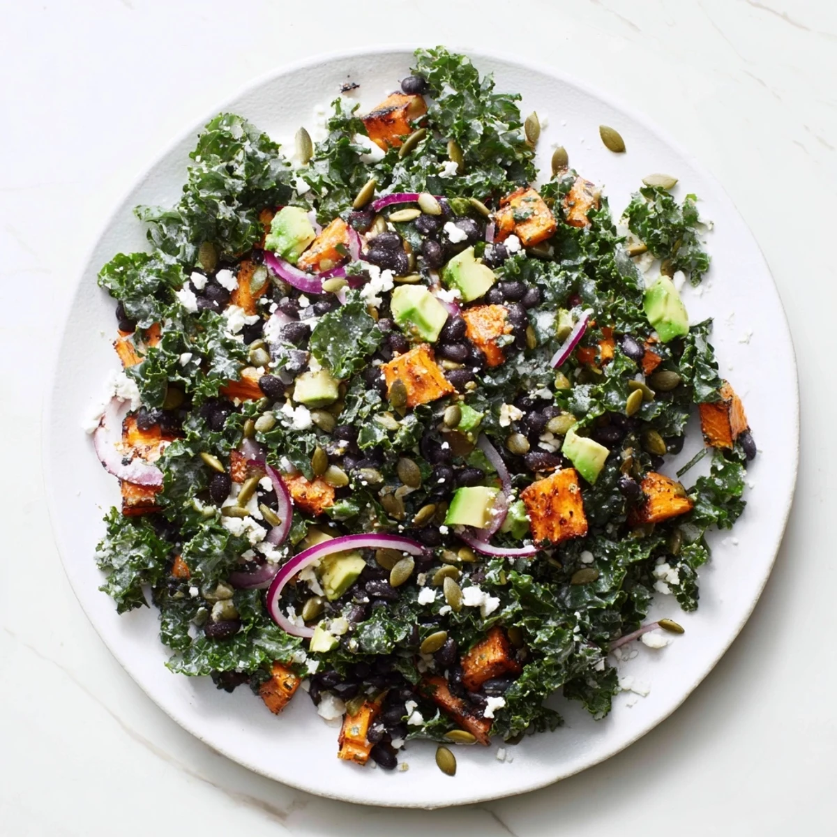 A bowl overflowing with massaged kale salad, featuring tender kale, black beans, and roasted sweet potato, ready to enjoy.