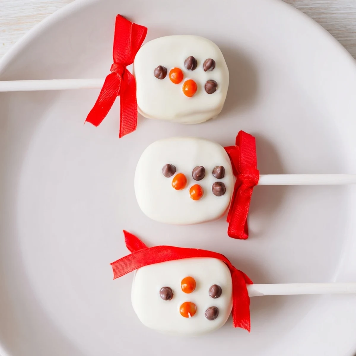 Homemade Express Snowman Marshmallow Pops, perfect for a winter treat; decorated with orange noses and candy scarves.