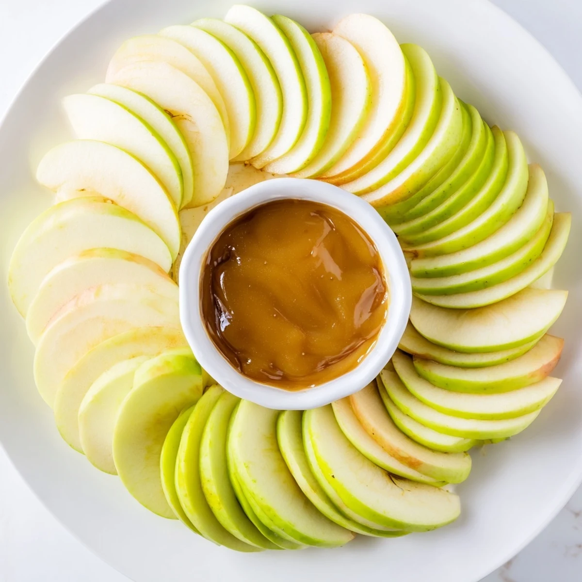 Fresh apple slices with a warm, glossy caramel dip center for easy snacking.