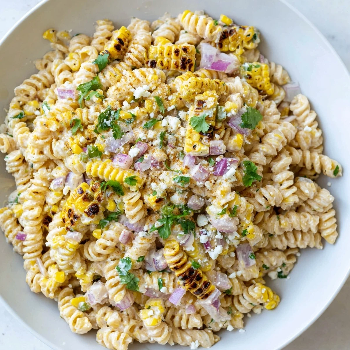 A bowl of Creamy Street Corn Pasta Salad garnished with fresh cilantro, perfect for a summer BBQ.