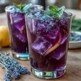 Refreshing lavender lemonade with fresh mint, served over ice with lemon slices and vibrant green garnish.