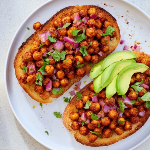 A close-up of BBQ chickpeas on toast, garnished with fresh herbs, a delicious, vegan meal.