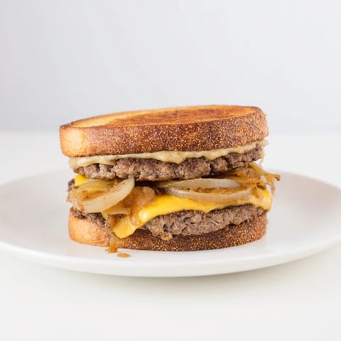 Close-up of a sizzling patty melt skillet showcasing perfectly melted cheese and caramelized onions.