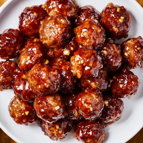Baked cherry-glazed meatballs, coated in a rich cherry sauce, served at a party with cocktail picks.