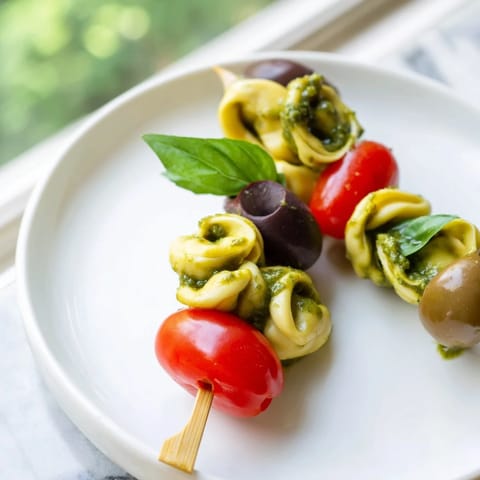 Italian-inspired Appetizer Skewers showcasing tortellini, pesto-coated, alongside olives and fresh basil on a platter.