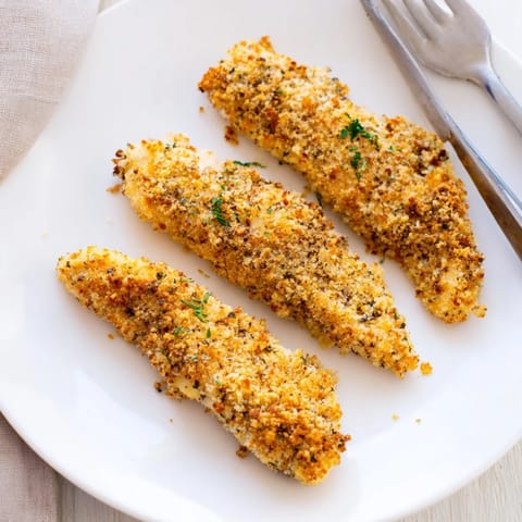 Freshly baked Crispy Panko Chicken Strips on a parchment-lined tray, showing a crunchy, golden texture perfect for casual gatherings.  