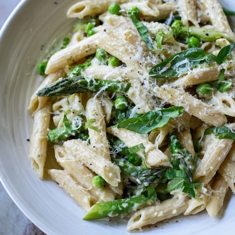 A close-up of Garlic Parmesan Spring Vegetable Pasta, garnished with fresh basil and extra grated Parmesan.