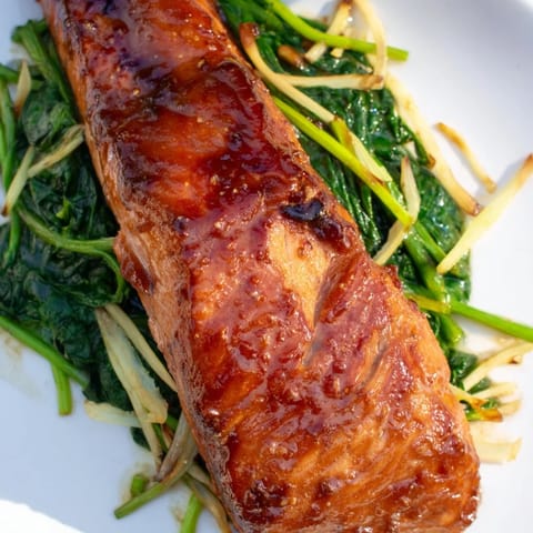 Perfectly seared miso salmon with a caramelized crust sits atop tender, garlic-infused sautéed spinach, ready for a nutritious weeknight dinner.  