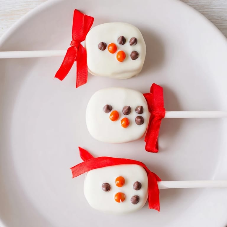 Homemade Express Snowman Marshmallow Pops, perfect for a winter treat; decorated with orange noses and candy scarves.