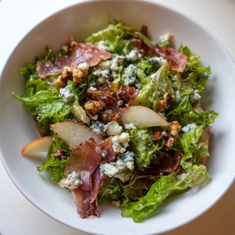 A close-up of the Frisée, Pear, Blue Cheese, and Crispy Prosciutto Salad shows a drizzle of tangy vinaigrette over the greens.